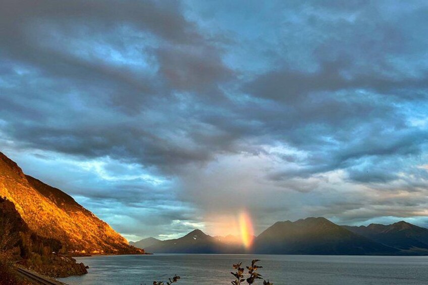 A mountainous landscape with a body of water, a rainbow, and a sunset. 3