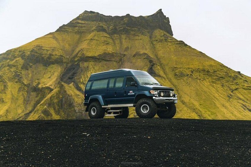 A blue SUV parked on a gravel road with a large, steep mountain in the background. 5