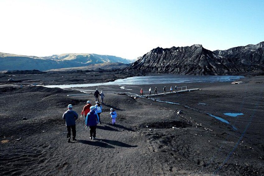 A group of people walking on a volcanic landscape with a body of water and mountains in the background. 2