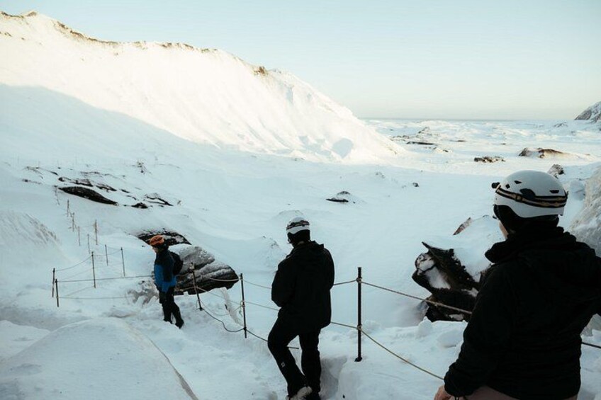 A snowy mountain landscape with a person in a blue jacket and orange helmet walking on a snow-covered path. 3