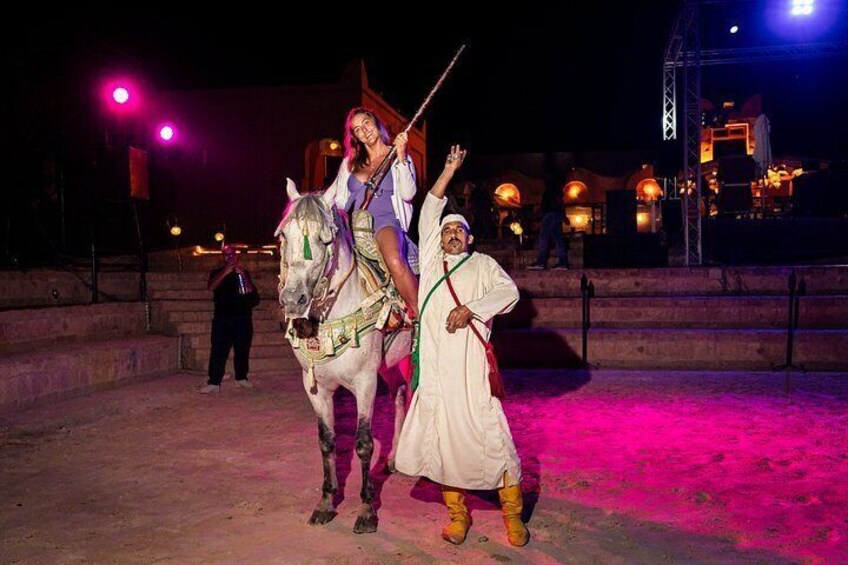 A person riding a horse, another person walking beside the horse, and a stage with lights in the background. 4