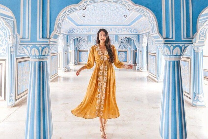 Une personne vêtue d’une robe dorée, dans une pièce aux éléments architecturaux bleus et blancs richement décorés. 1