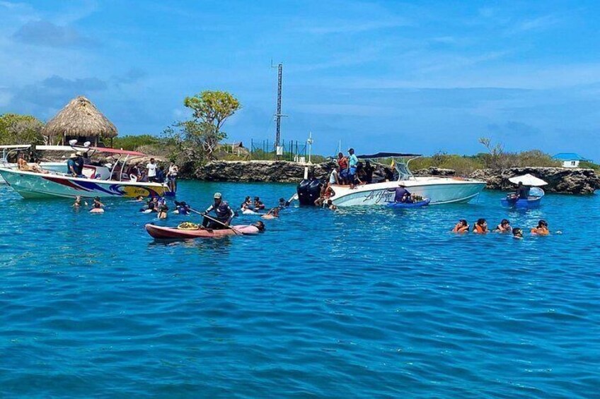 Un grupo de personas en un bote, algunas en el agua, y una cabaña con techo de paja al fondo. 4