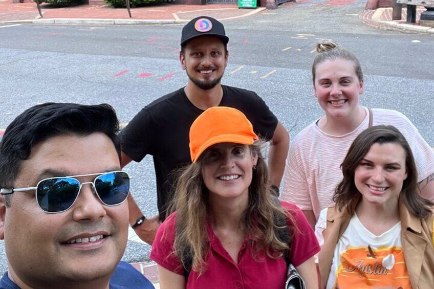 A group of people standing on a street with a road in the background. 1