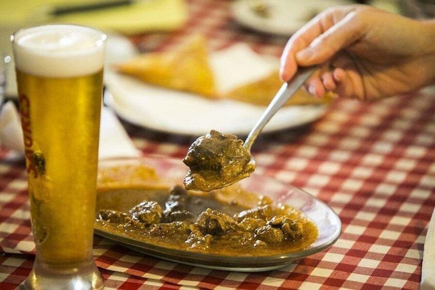 Un verre de bière, une cuillère de curry et une assiette de nourriture sur une nappe à carreaux. 3