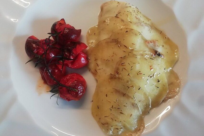 Un piatto con un pezzo di pollo ricoperto di salsa e guarnito con erbe aromatiche, accompagnato da pomodori rossi arrostiti. 2