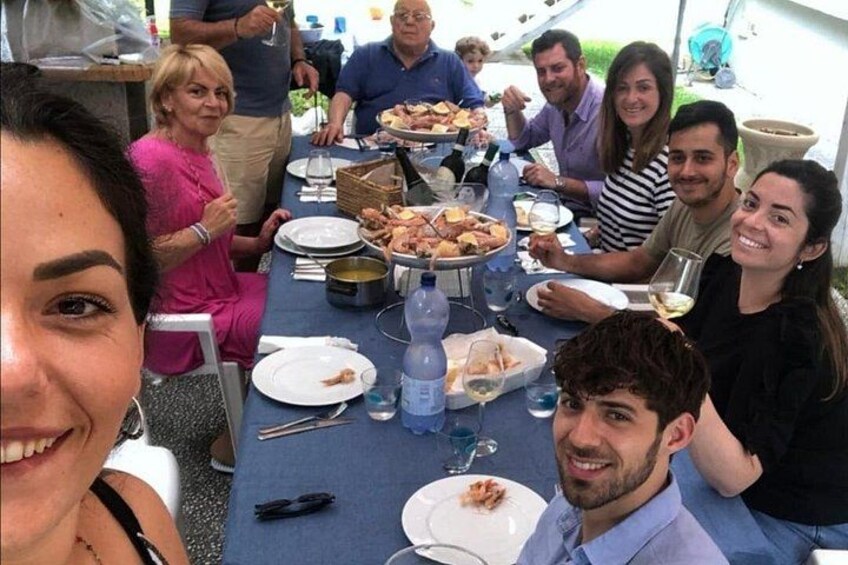 Un gruppo di persone sedute attorno a un tavolo con cibo e bevande, all'aperto. 1