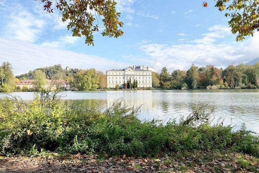 Ein See mit einem Gebäude im Hintergrund, umgeben von Bäumen und Vegetation. 3