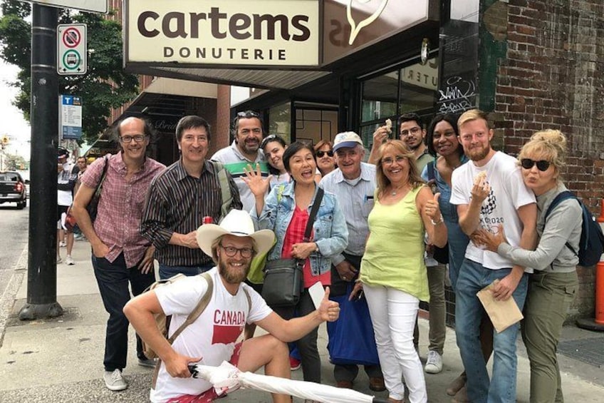 A group of people posing in front of a bakery named 'cartems Donuterie.' 2