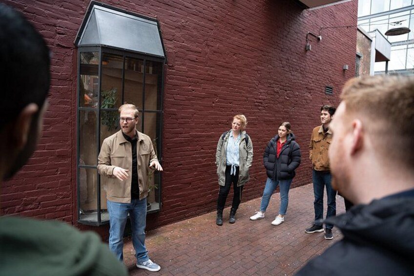 A group of people standing in an alleyway with a red brick building and a glass door. 3