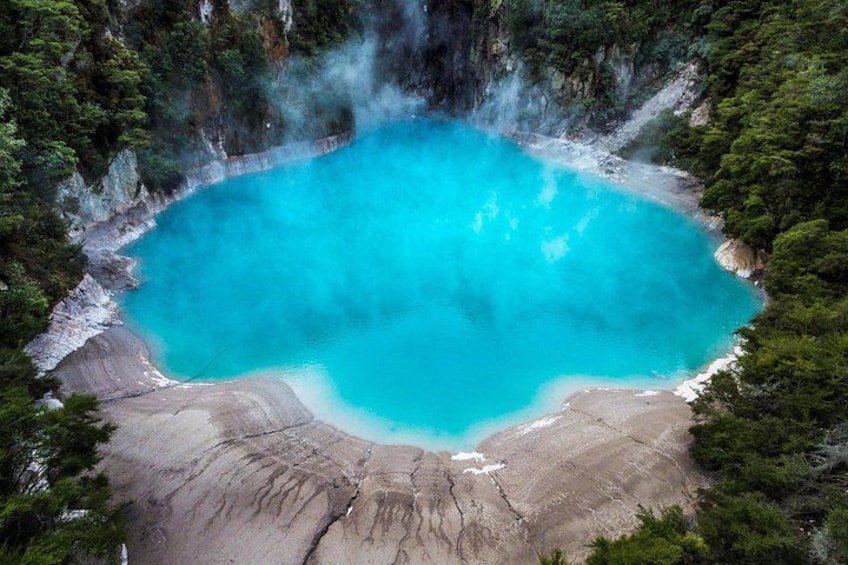Ein türkisfarbenes Thermalbad, umgeben von bewaldeten Klippen. 1