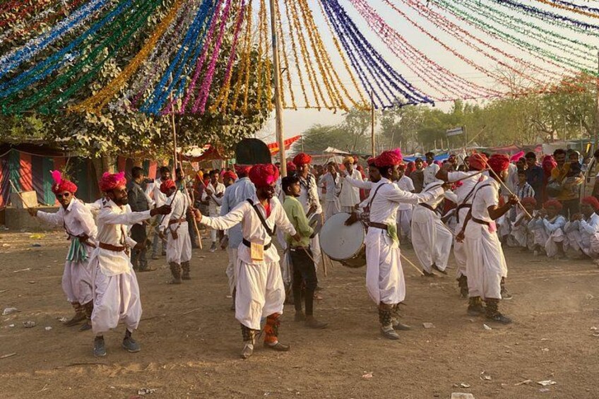 A group of men in traditional attire performing a dance with drums in an outdoor setting. 5