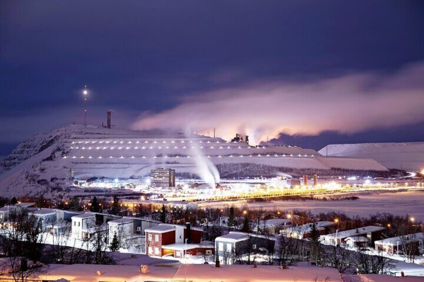 A snow-covered landscape with a large illuminated structure and a building with a red roof. 1