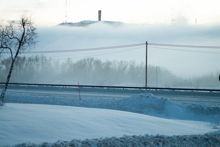 A snow-covered landscape with a road, a power line, and a distant hill with a structure. 3