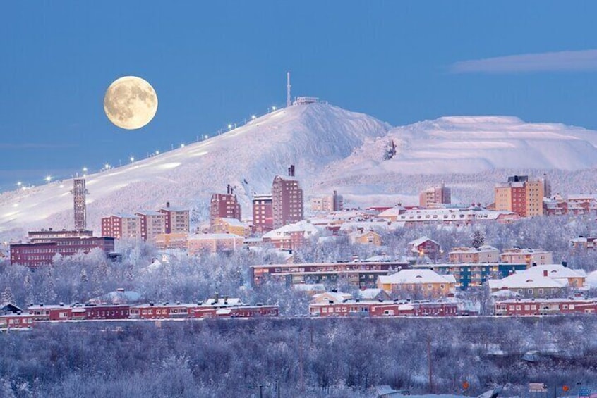 A snow-covered cityscape with a prominent mountain in the background and a full moon in the sky. 3