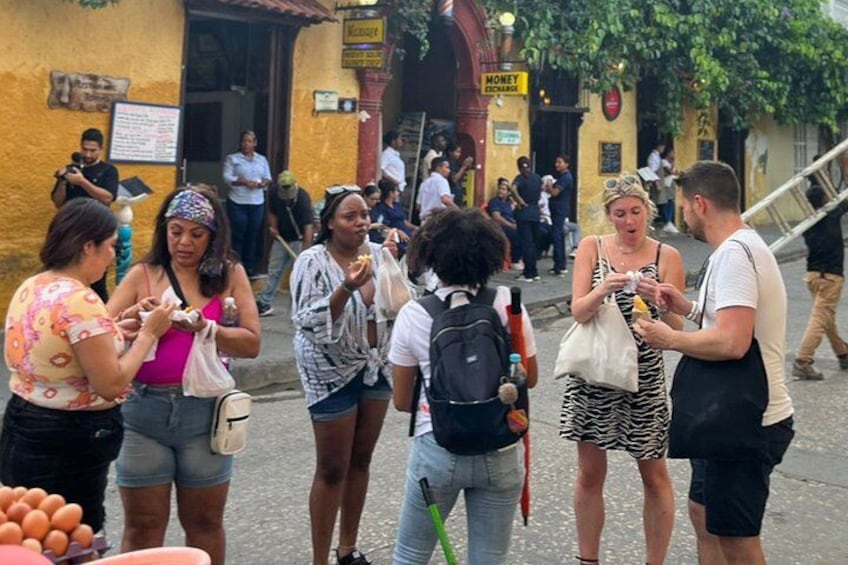 A group of people standing and conversing on a street with buildings and a staircase in the background. 2