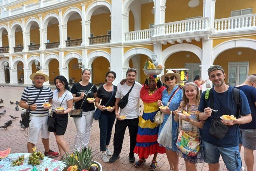 A group of people standing in a courtyard with yellow and white architecture, holding plates of food. 4