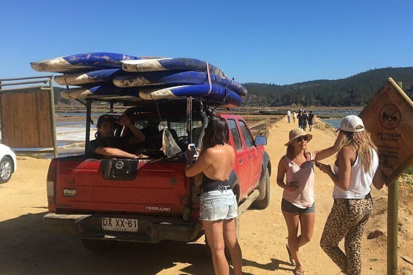 A red truck with surfboards on the back, people standing beside it, and a sign with a no swimming warning. 4