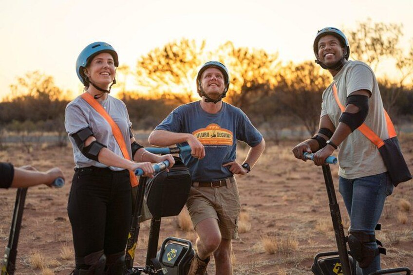 Three people riding electric scooters in an open area with trees in the background. 3