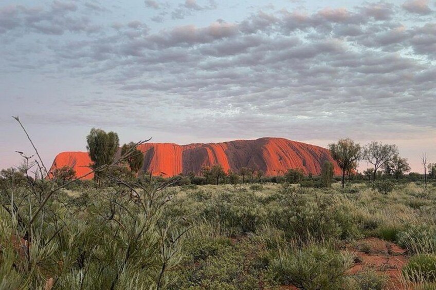 A large red rock formation in a natural landscape with sparse vegetation. 2