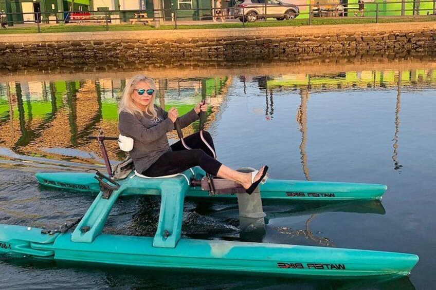 A person sitting on a green paddle boat on a calm body of water. 1