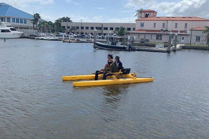 A yellow raft with two people on a calm body of water, surrounded by buildings and boats. 3