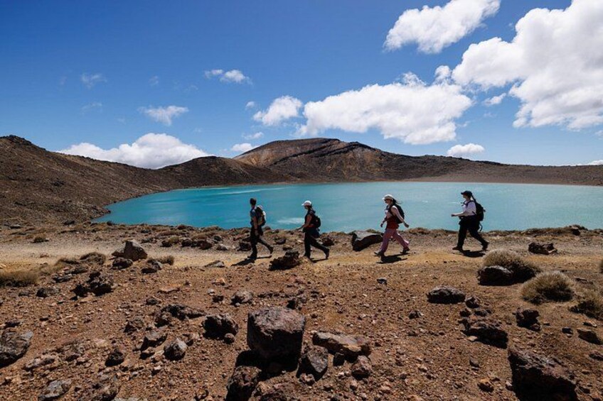 A group of hikers walking on a rocky terrain with a lake and mountains in the background. 3