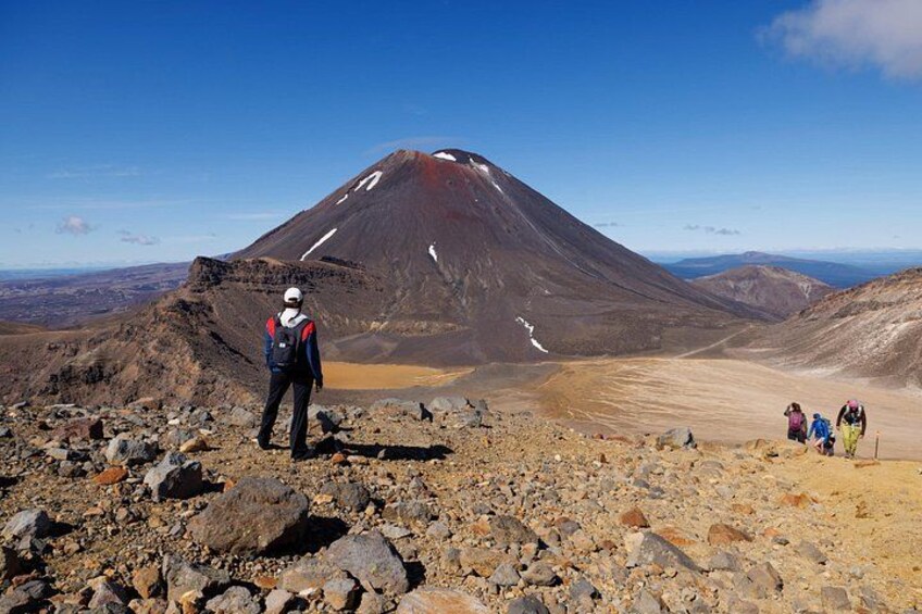 A mountainous landscape with a person standing on rocky terrain and a group of people in the distance. 5