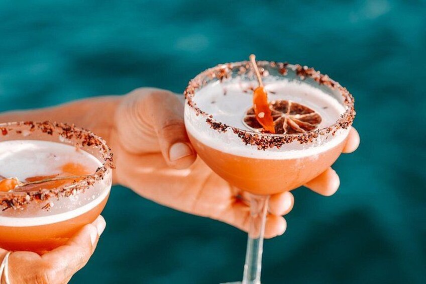 Two cocktail glasses with a salted rim and a star anise garnish, held by a person against a blue background. 3