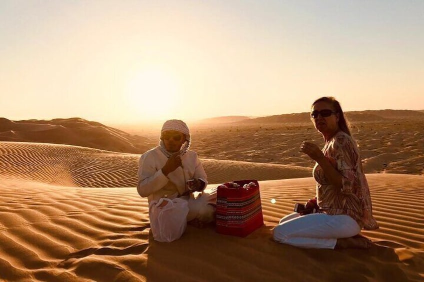 Two people sitting on sand dunes during sunset. 1