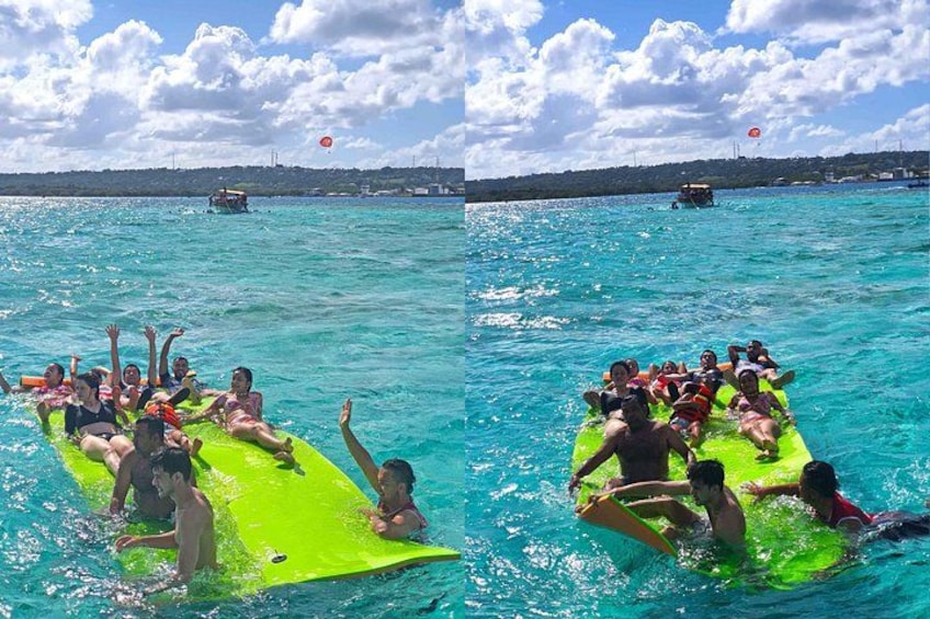 Des personnes se trouvent sur un radeau vert, au milieu d’une mer turquoise, avec des bateaux en arrière-plan. 5