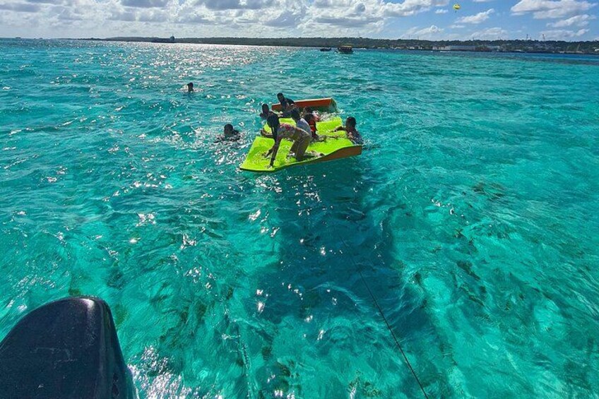 Des personnes se trouvent sur un radeau vert, dans une eau turquoise et cristalline. 2