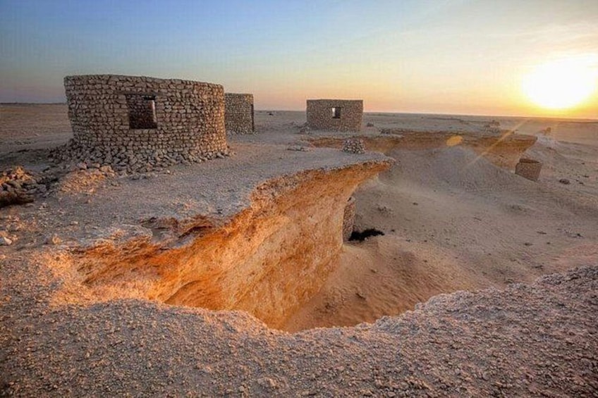 A desert landscape with a large sinkhole, stone structures, and a sunset. 2