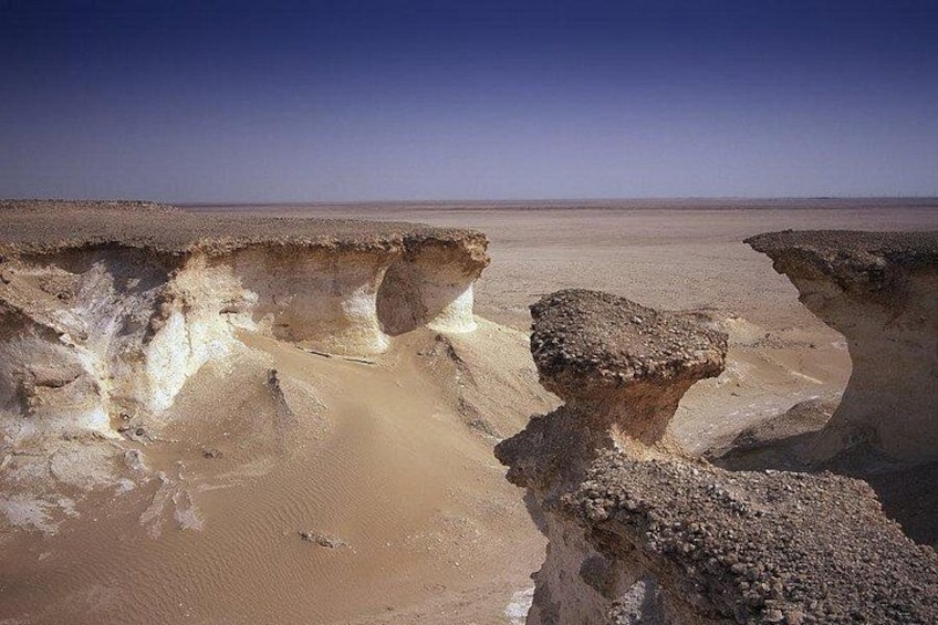 A desert landscape with a prominent rock formation and a large sinkhole. 3