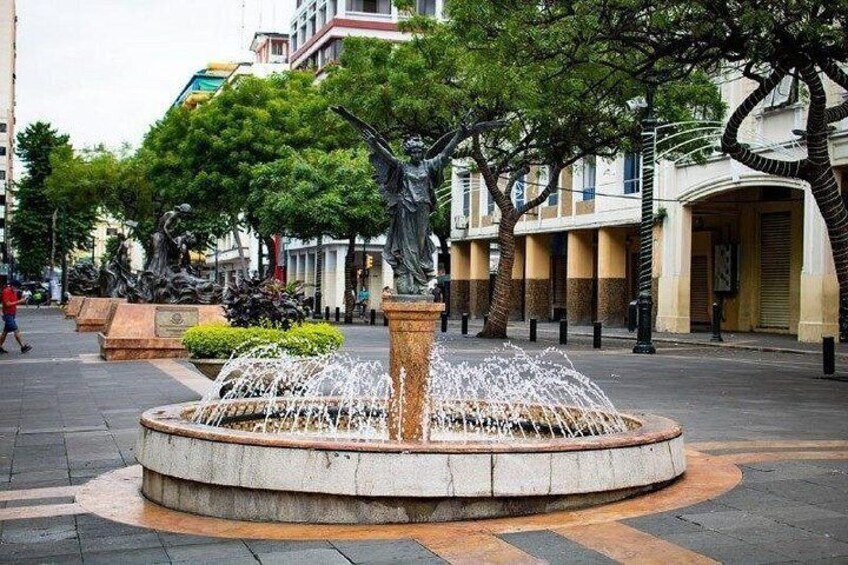 A circular fountain with water jets, surrounded by trees and buildings. 1