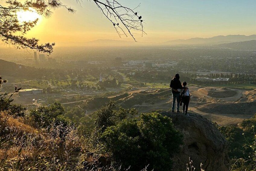 Una pareja parada en una colina con vistas a un paisaje urbano al atardecer. 2