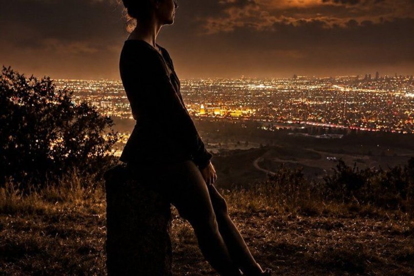 A person sitting on a rock overlooking a cityscape at night. 5