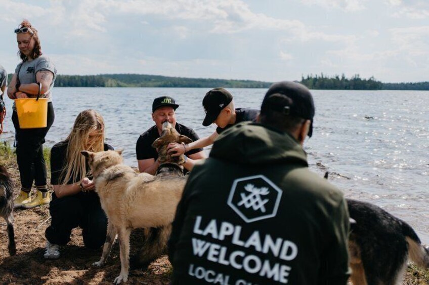 A group of people by a lake, some wearing 'Lapland Welcome' jackets. 2