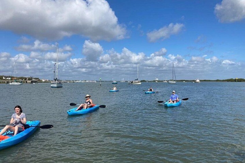 People kayaking on a calm body of water with sailboats in the background. 3