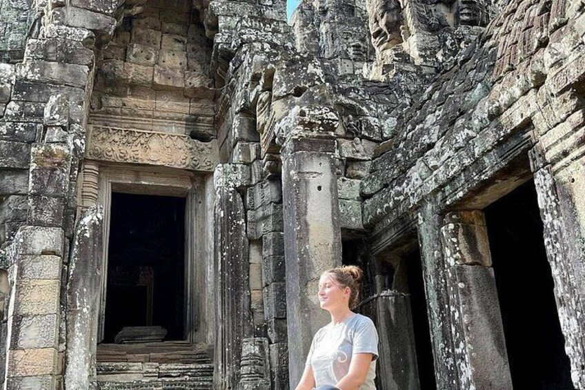 A woman standing in front of an ancient stone structure with intricate carvings and a doorway. 5