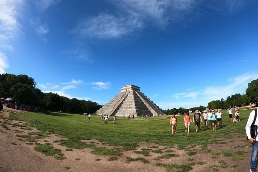 A large pyramid structure surrounded by a grassy field with people walking around. 2