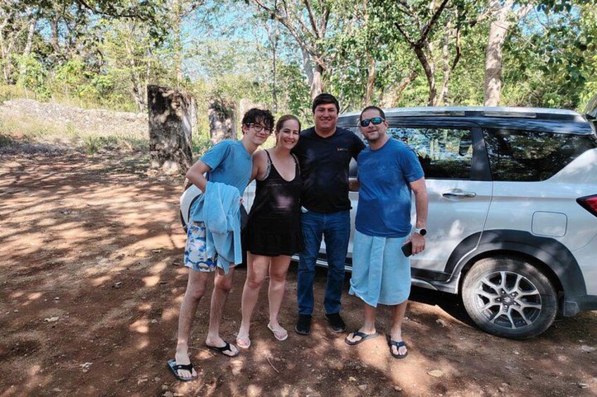 Four people standing outdoors with a vehicle in the background. 1