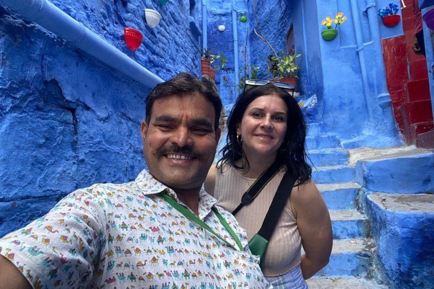 Ein schmaler Gang mit blauen Wänden und roten Hauseingängen, eine Person macht ein Selfie. 3