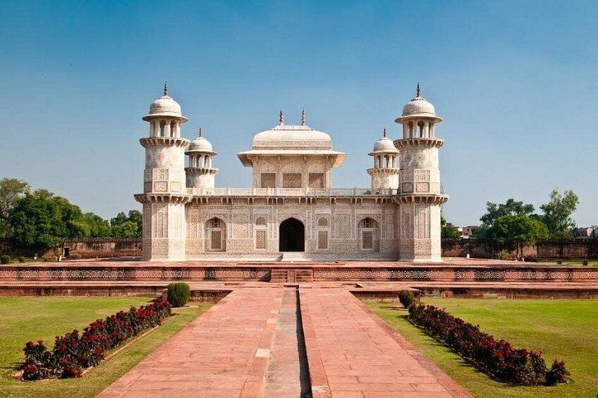 A large white marble building with domes and minarets, surrounded by a well-maintained garden and a paved pathway. 3