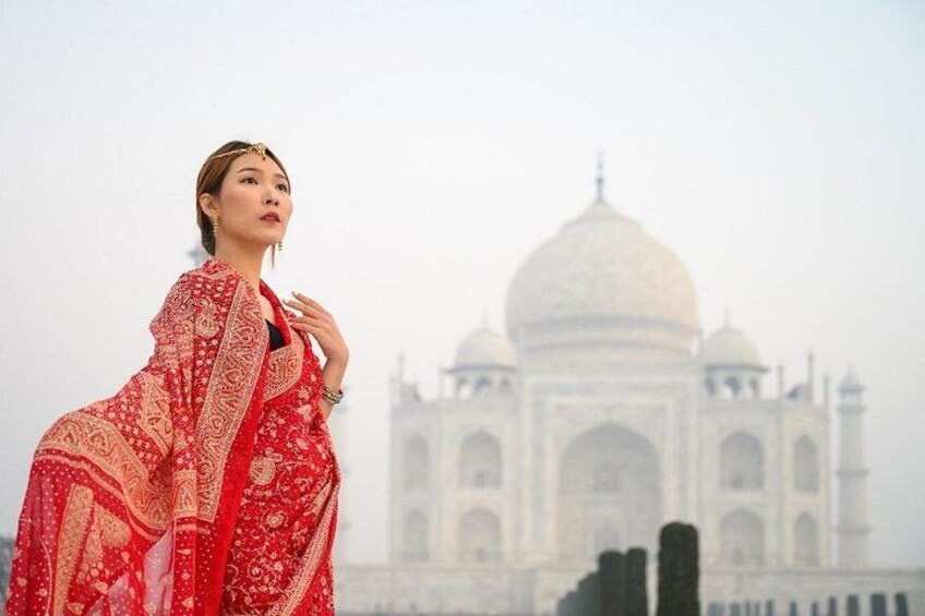 A person in a red traditional outfit standing in front of the Taj Mahal. 2