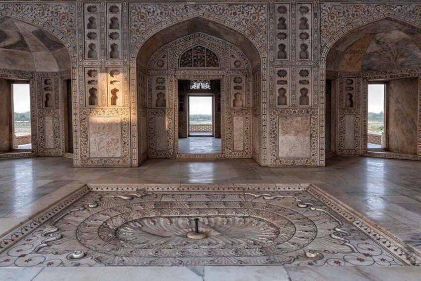 An ornate interior with intricate carvings, a large circular carpet, and a view through an archway. 2