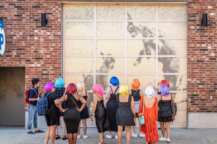 Un groupe de personnes se tient devant un bâtiment dont la grande fenêtre laisse voir une fresque murale. 5