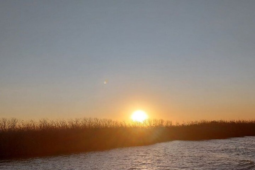 A sunset over a body of water with a silhouette of a grassy area in the foreground. 2