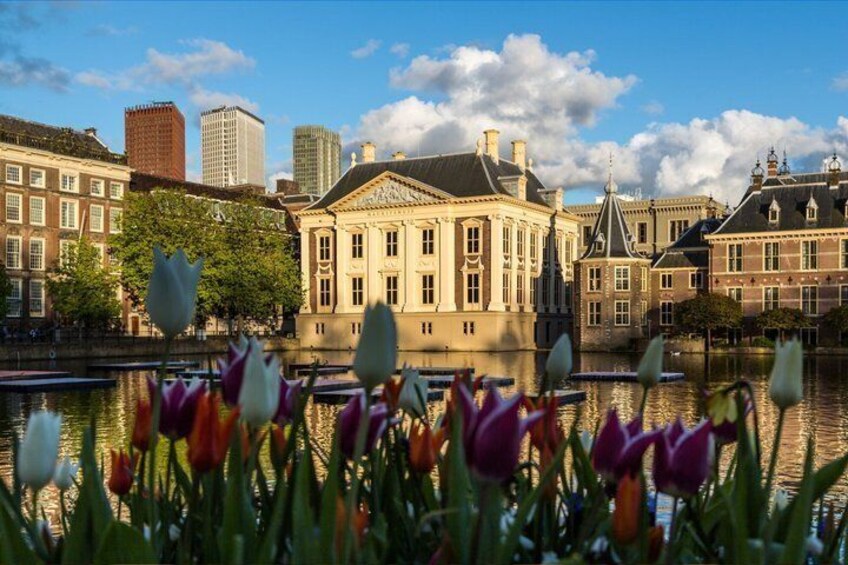A historic building with a pond in front, surrounded by tulips and modern skyscrapers in the background. 1