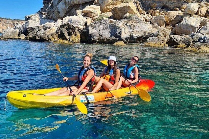 Three people kayaking on clear water with a rocky shoreline in the background. 4